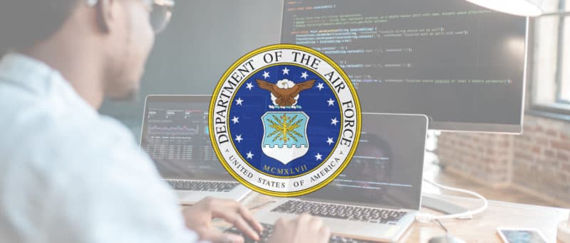 A man working at a computer with code displayed on the screen. There is a white overlay with the U.S. Air Force seal in the middle