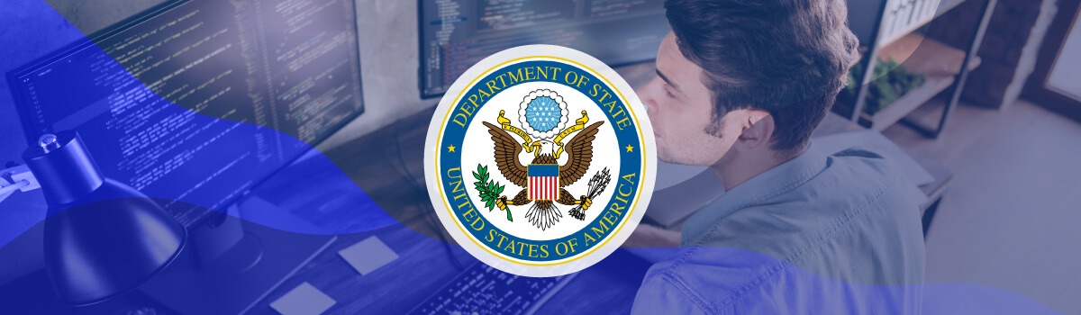 a man working at a desk with two monitors displaying code with the Department of State seal overlaid on the image
