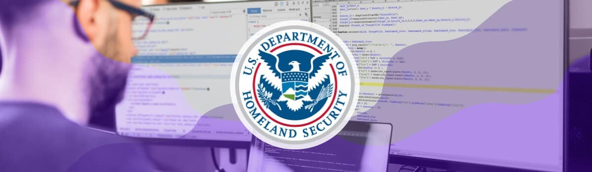 A man working at a desk with a laptop and two monitors reviewing code, the U.S. Department of Homeland Security seal is overlaid on top